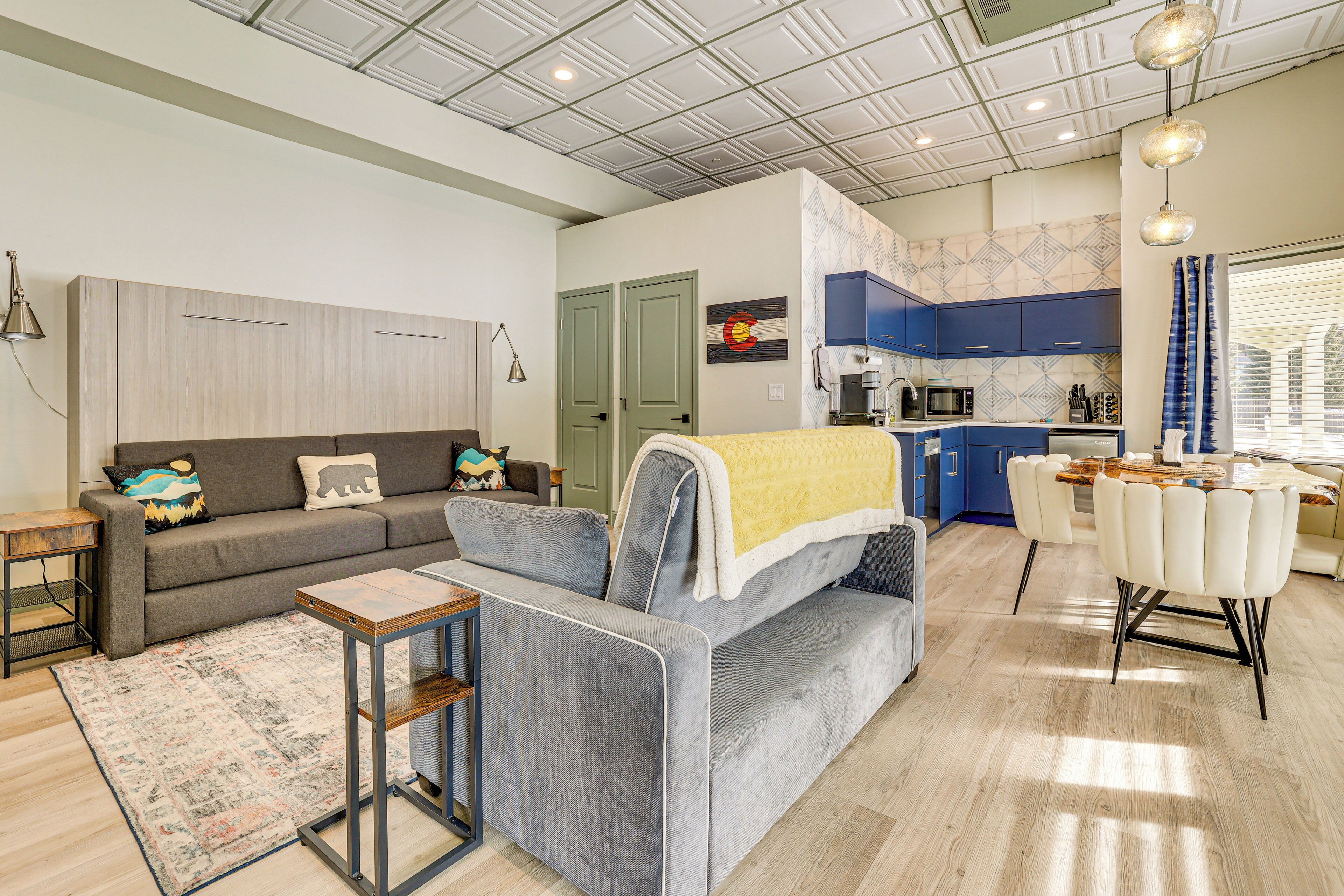 Ein modernes Wohnzimmer mit grauem Sofa, einem Couchtisch und einem Essbereich mit weißem Tisch und Stühlen.