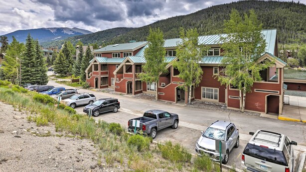 A multi-story building with a red brick facade and green roofs, surrounded by parked cars and trees, with mountains in the background. - Keystone Lake Haven: Heated Pool & Ski Shuttle! (Keystone)