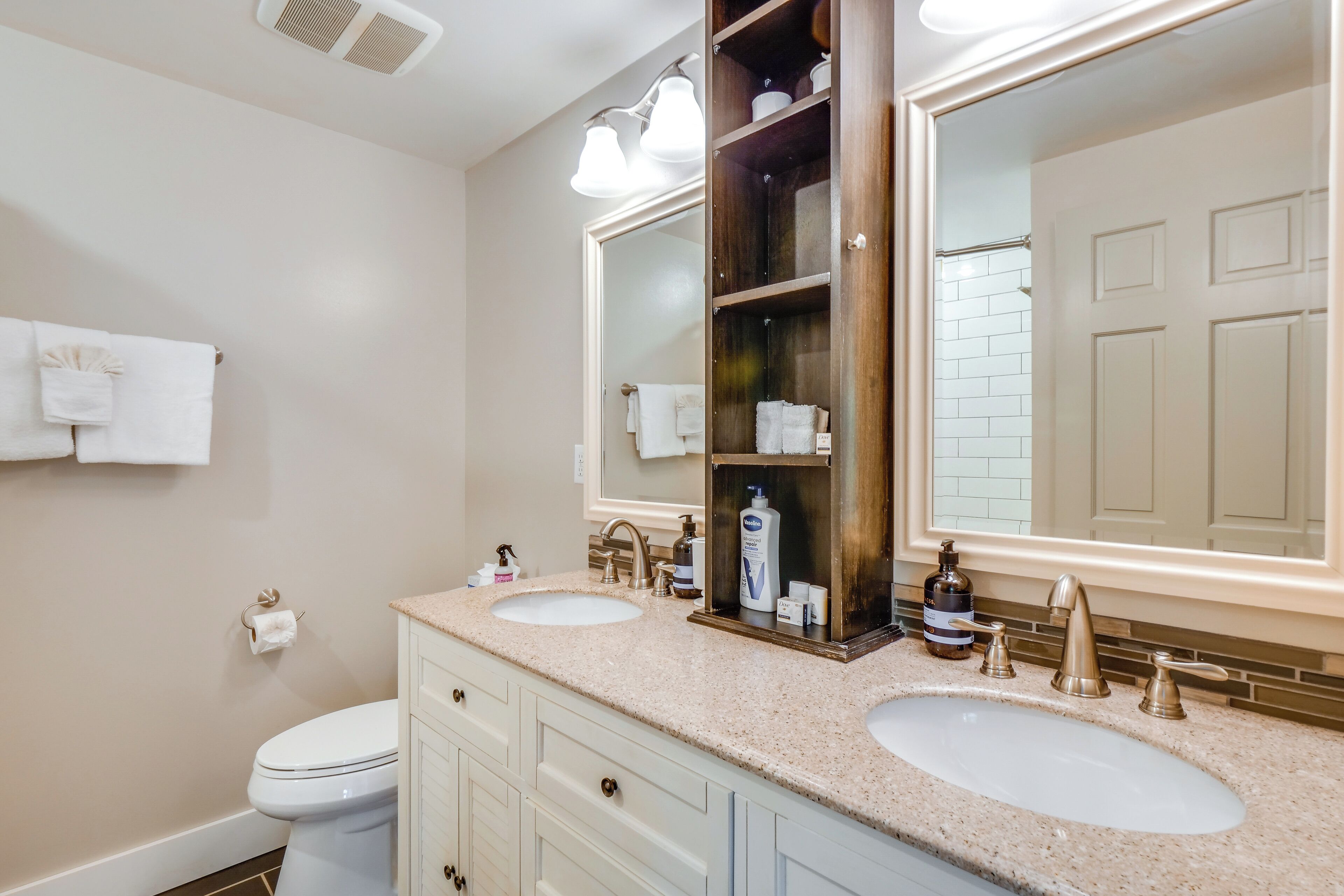 A bathroom with two sinks, a toilet, a large mirror, and a towel rack.