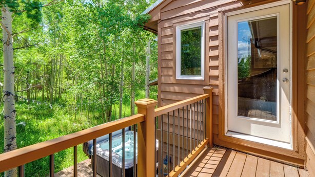 A wooden deck with a hot tub, a glass door, and a view of a forest.