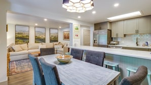 A modern kitchen with a central island, dining area with chairs, and a sofa.