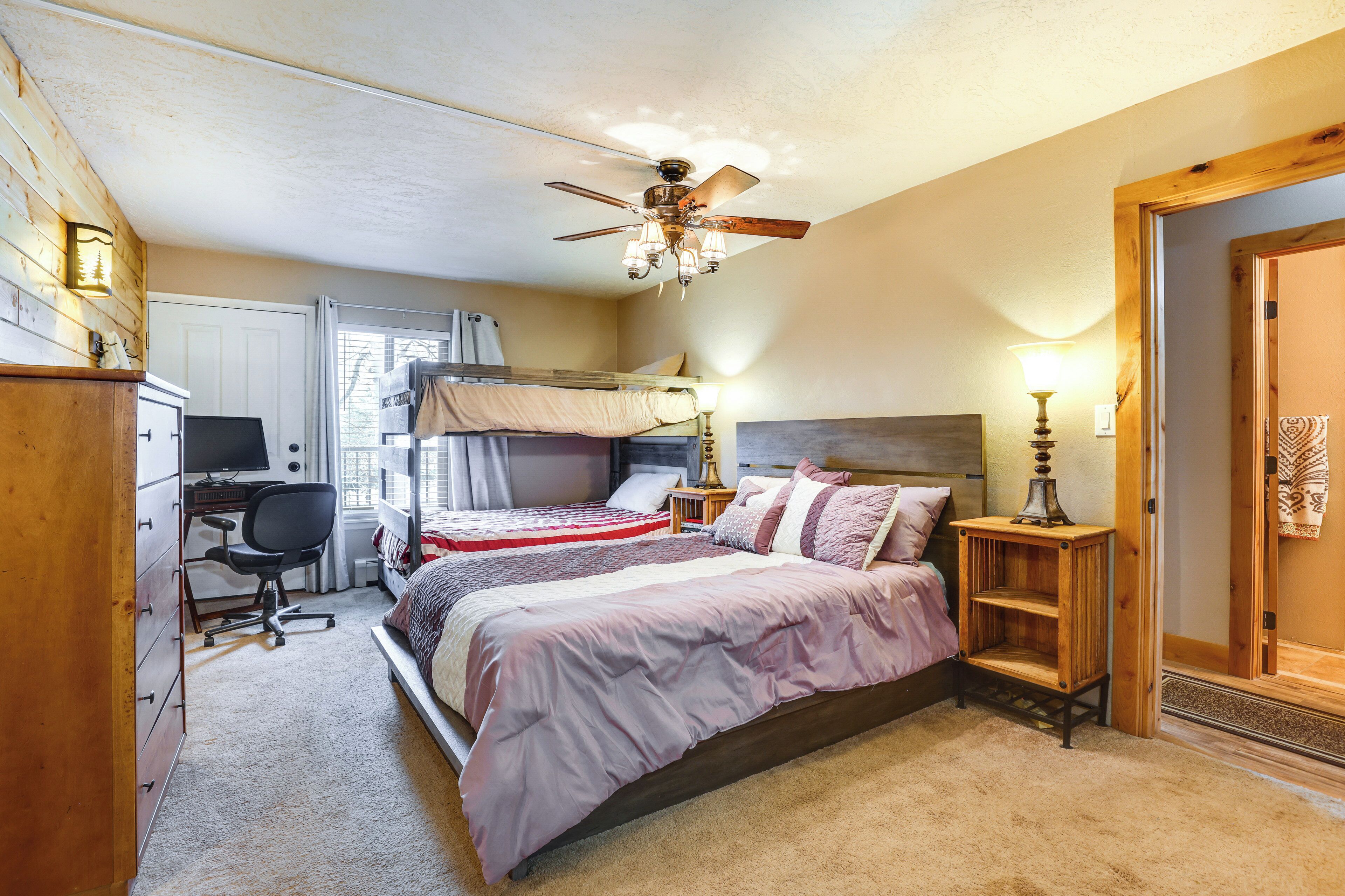 A bedroom with a bunk bed, a desk, a chair, a lamp, and a ceiling fan.