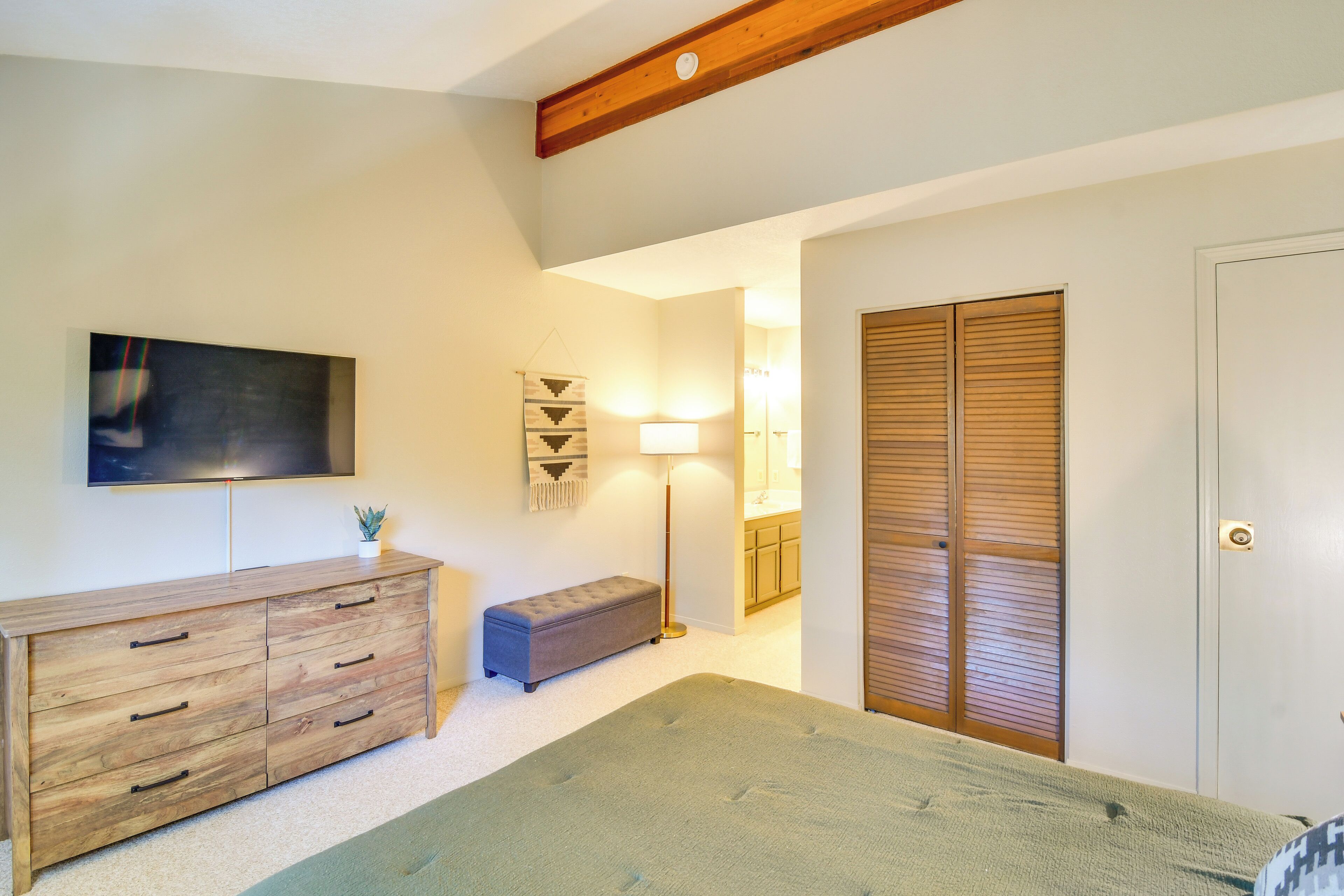A bedroom with a bed, a dresser, a bench, a TV, a lamp, and a closet.