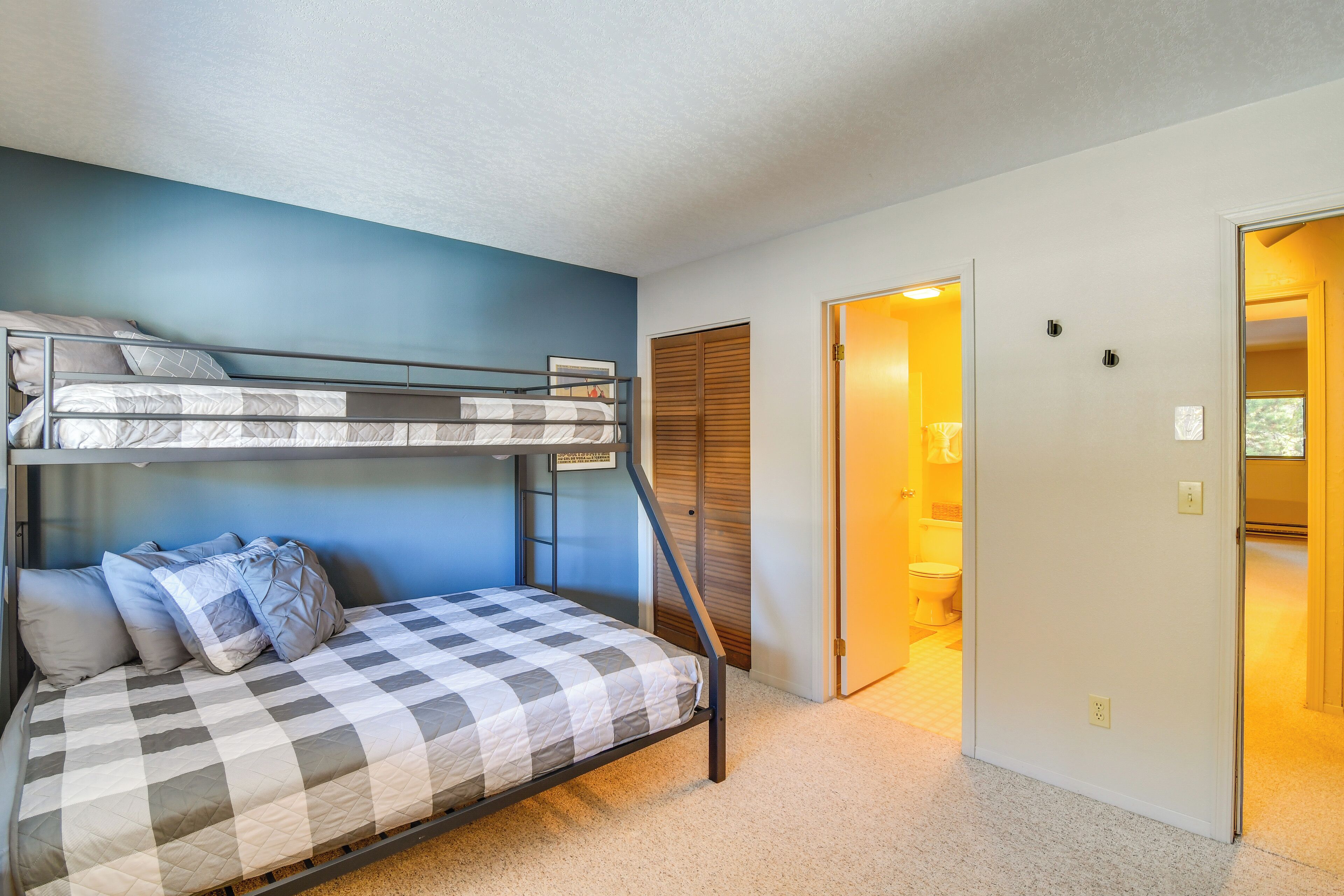 A bunk bed with a checkered bedspread and pillows, a blue accent wall, and a door leading to a bathroom.