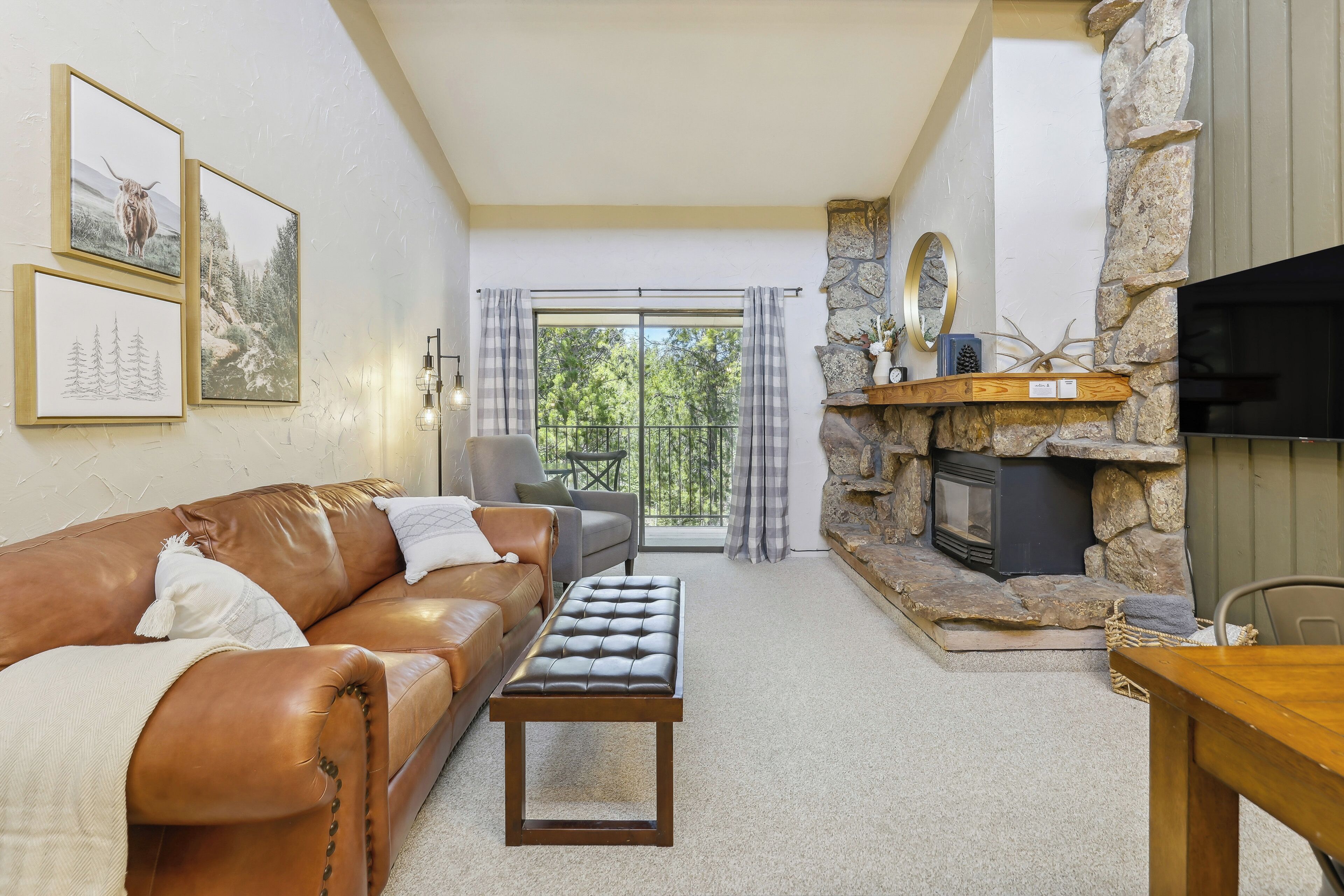 A cozy living room with a leather sofa, a wooden coffee table, a stone fireplace, and framed pictures on the wall.