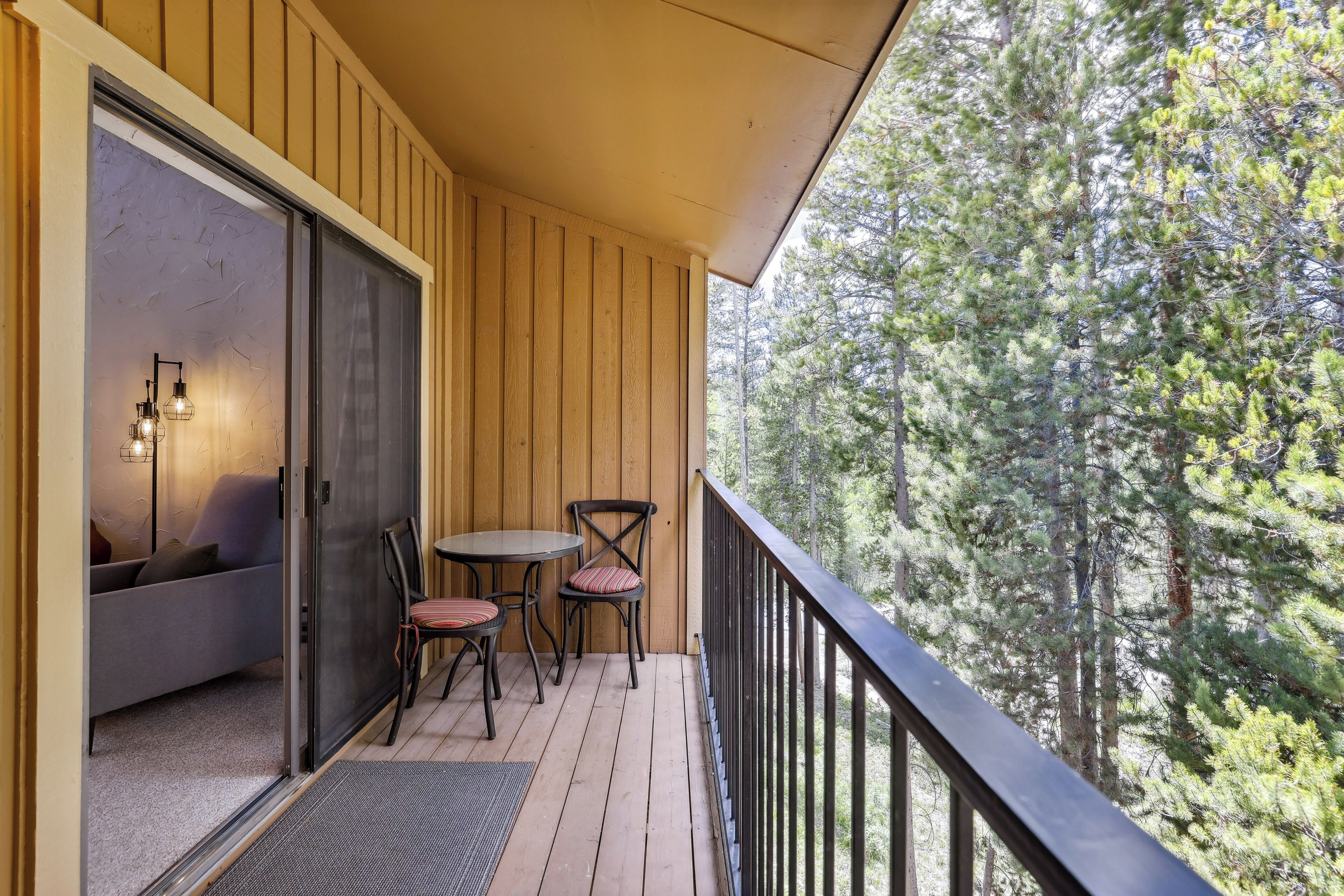 A wooden deck with a sofa and two chairs, a glass door, and a view of trees.