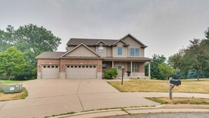 A two-story house with a garage, a front porch, and a driveway leading to the garage. - Prime Peoria Retreat w/ Deck & Fireplace! (Peoria)