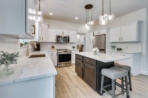 A modern kitchen with white cabinetry, stainless steel appliances, and a central island with bar stools. - Prime Peoria Retreat w/ Deck & Fireplace! (Peoria)