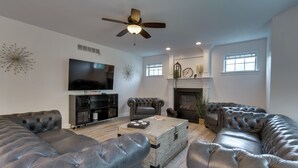 A modern living room with leather sofas, a flat-screen TV, a fireplace, and a ceiling fan. - Prime Peoria Retreat w/ Deck & Fireplace! (Peoria)