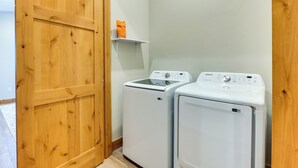 A laundry room with two white front-loading washing machines and a wooden door. - Mountain-view Fraser Condo w/ Balcony + Hot Tub! (Fraser)