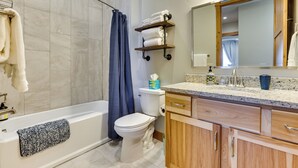 A modern bathroom with a bathtub, toilet, and shower. There are towels on the wall and a shelf with more towels. The bathroom has wooden cabinets and a large mirror. - Mountain-view Fraser Condo w/ Balcony + Hot Tub! (Fraser)