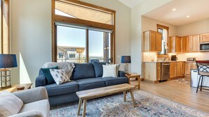 A modern living room with a sofa, a coffee table, and a view of the kitchen. - Mountain-view Fraser Condo w/ Balcony + Hot Tub! (Fraser)