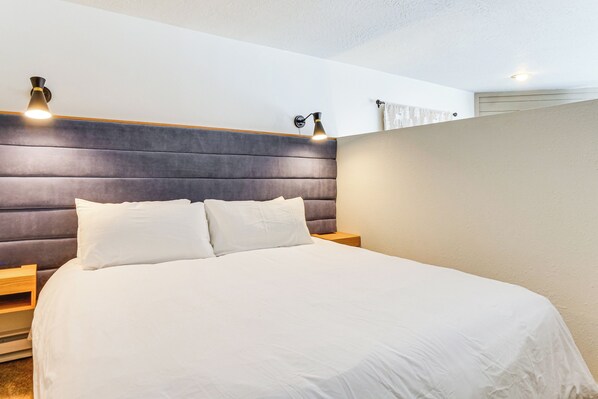 A neatly made bed with white linens, a dark headboard, and two bedside lamps.