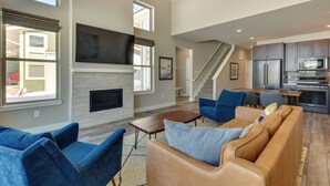 A spacious living area with a fireplace, modern furniture, and a kitchen in the background. - Fraser Vacation Rental - Shuttle to Winter Park! (Fraser)