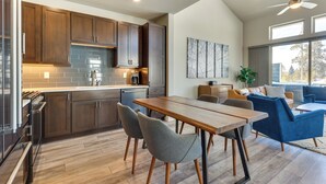 A modern kitchen with wooden cabinets, a dining area with a wooden table and chairs, and a living area with a sofa and a plant. - Fraser Vacation Rental - Shuttle to Winter Park! (Fraser)