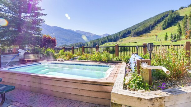 Ein Whirlpool mit einer Holzterrasse, umgeben von einem Holzzaun und üppiger Vegetation, mit Blick auf eine gebirgige Landschaft.