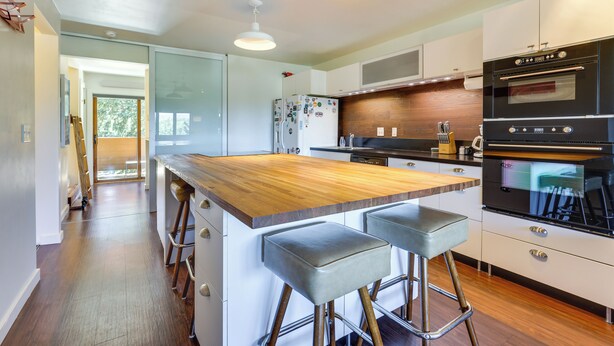 A modern kitchen with a wooden island, bar stools, a refrigerator, and built-in ovens. - Winter Park Condo w/ Private Balcony: Near Skiing! (Winter Park)