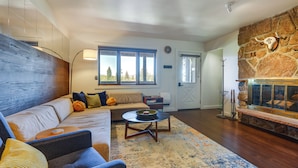A modern living room with a stone fireplace, a sofa, a coffee table, and a large window with a view of trees. - Winter Park Condo w/ Private Balcony: Near Skiing! (Winter Park)