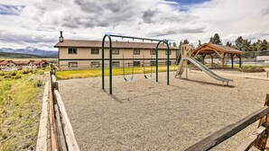 A playground with swings and a slide, a covered seating area, and a building with a sloped roof in the background. - Fraser Condo Rental w/ Balcony, Mountain Views! (Fraser)