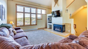 A living room with a large window, a fireplace, a television, and a sofa. - Winter Park Condo Rental: 4 Mi to Ski Resort! (Winter Park)