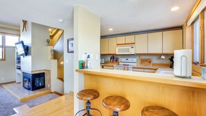 A modern kitchen with wooden cabinets, a microwave, and a built-in oven. There are two stools at the counter and a fireplace in the corner. - Winter Park Condo Rental: 4 Mi to Ski Resort! (Winter Park)