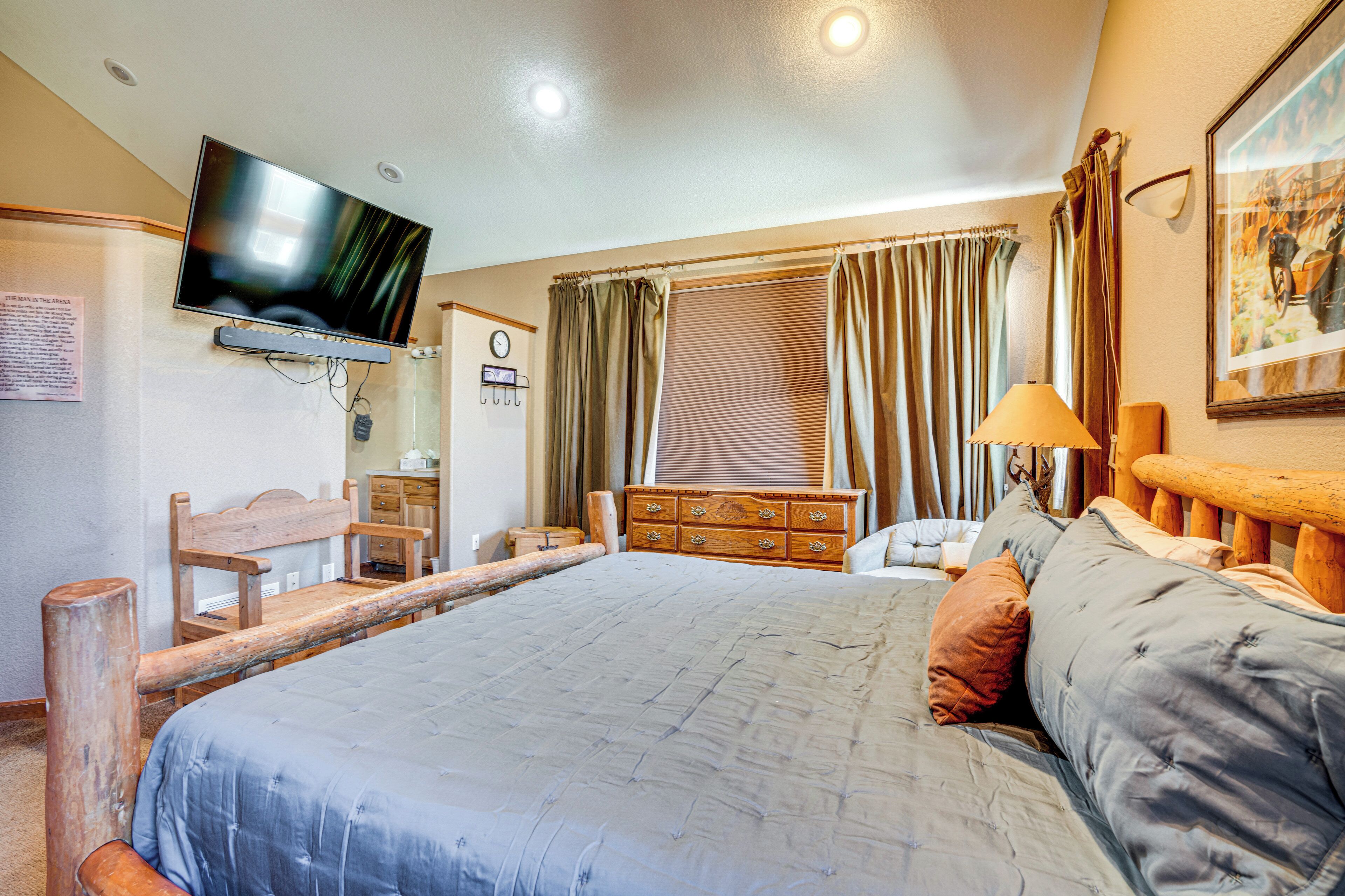 Una camera da letto con un letto grande, una televisione montata a parete, una testiera in legno, un comò di legno e una finestra con tende.