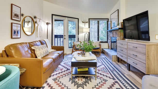 A living room with a brown leather sofa, a coffee table with a plant, a TV on a wooden cabinet, and a patterned rug. - Pool + Ski-in Access: Copper Mountain Condo! (Copper Mountain)