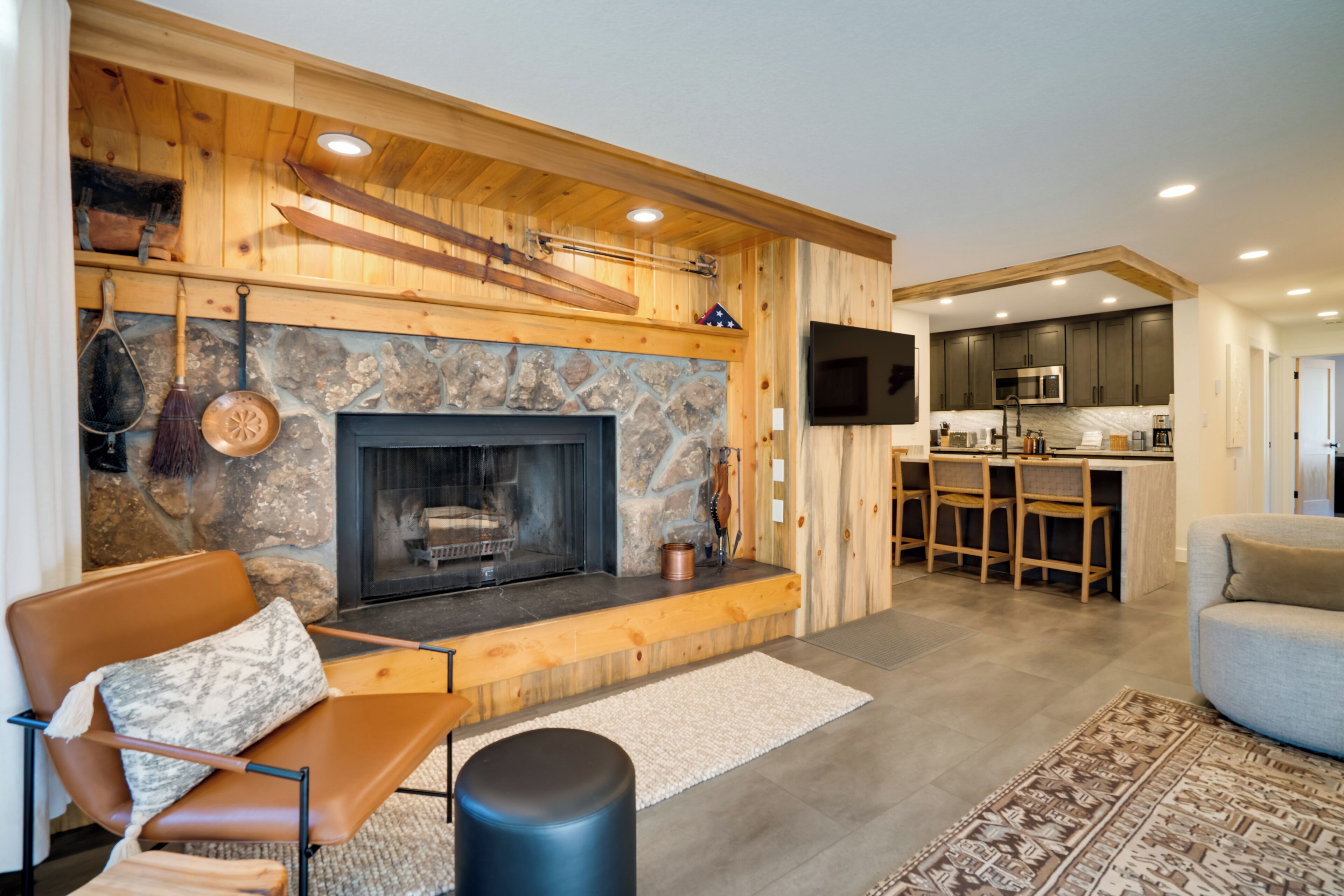 A modern living room with a stone fireplace, wooden beams, and a bar area with stools.