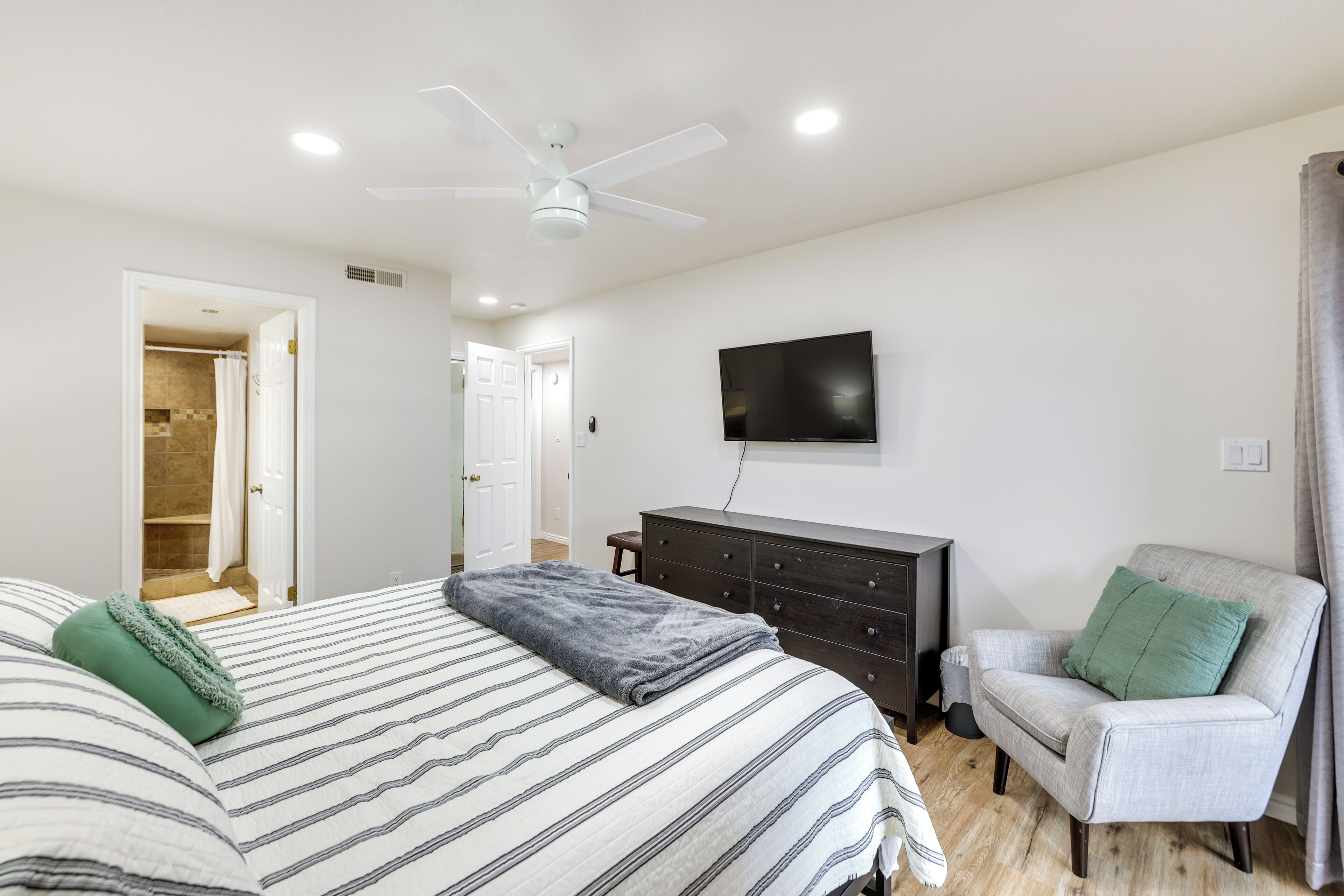 Un dormitorio con cama, cómoda, silla, televisor y ventilador de techo.