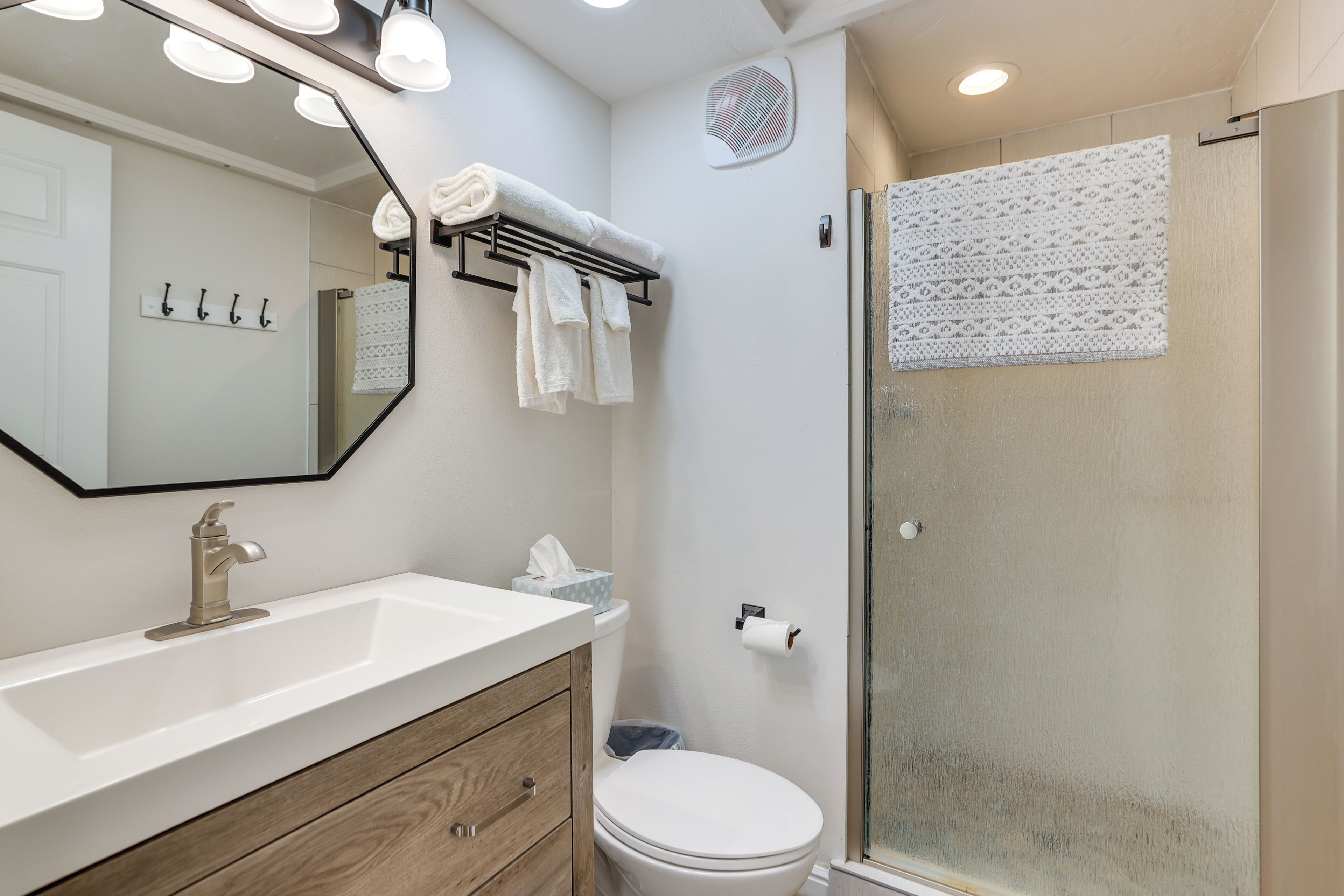 Een badkamer met een witte wastafel, een spiegel, een handdoekhouder, een toilet en een douchecabine van glas.