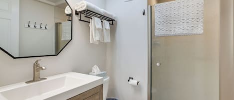 A bathroom with a white sink, a mirror, a towel rack, a toilet, and a glass shower enclosure.