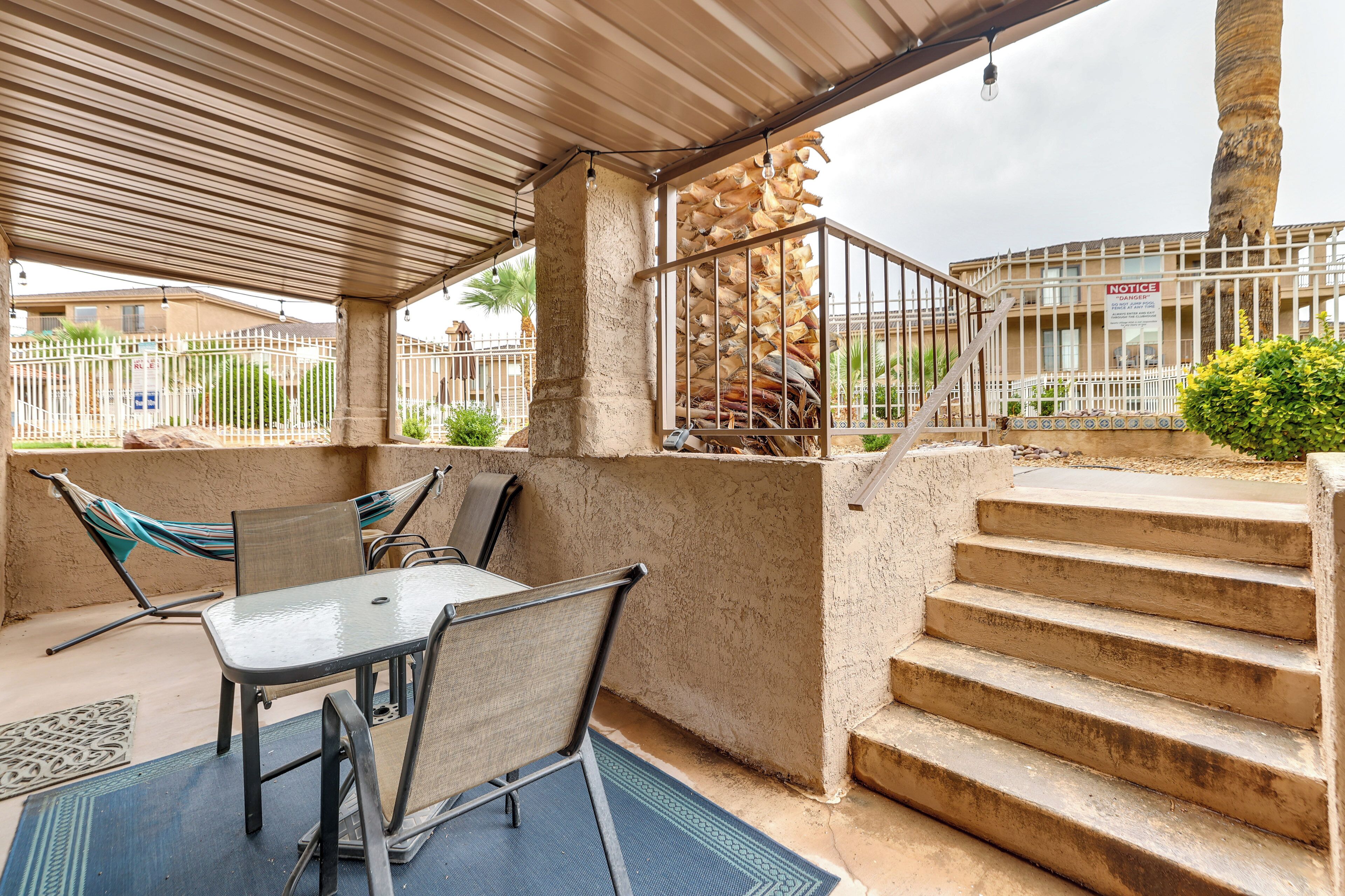 A covered outdoor area with a table and chairs, a hammock, and a staircase leading to a building with a 'Danger' sign.