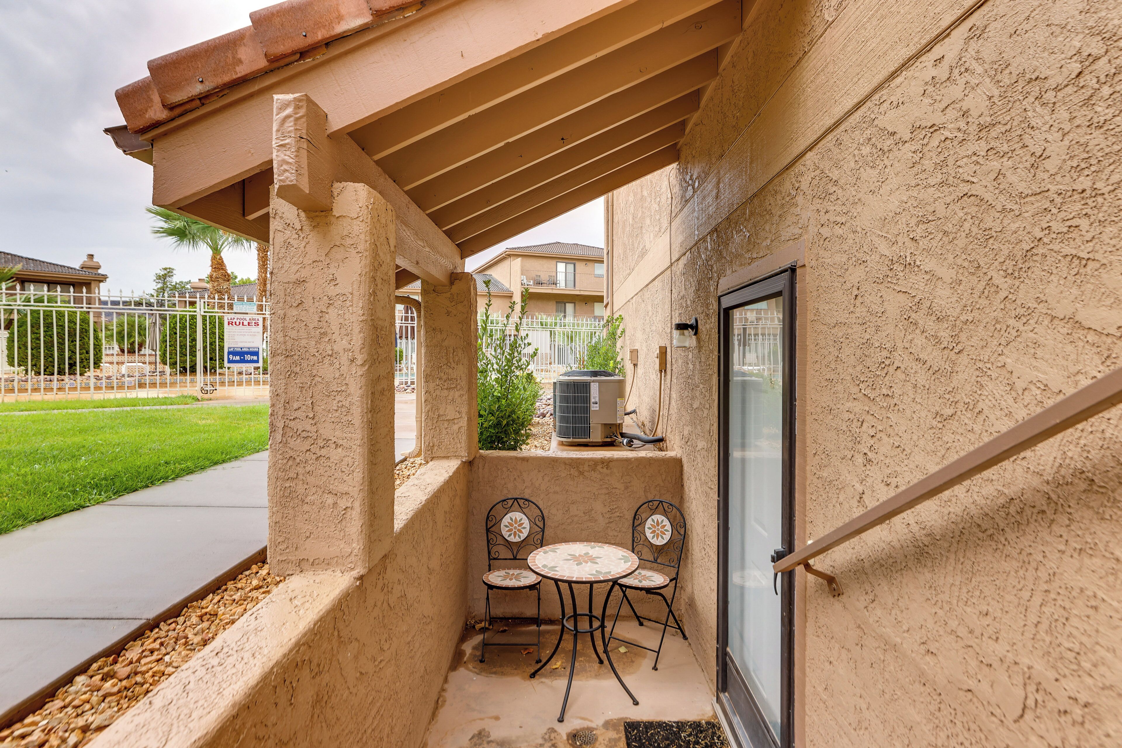 A covered patio area with a table and two chairs, a door, and a view of a residential area.