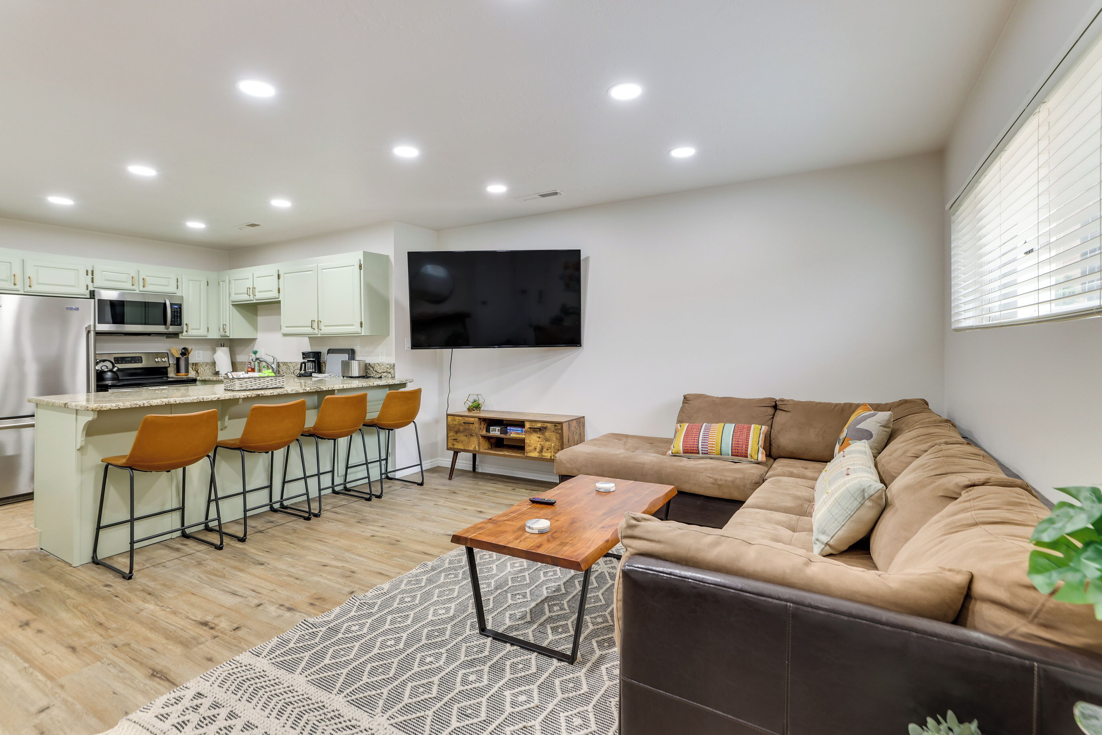 A modern kitchen with a central island, a dining area with chairs, a sofa, and a TV mounted on the wall.