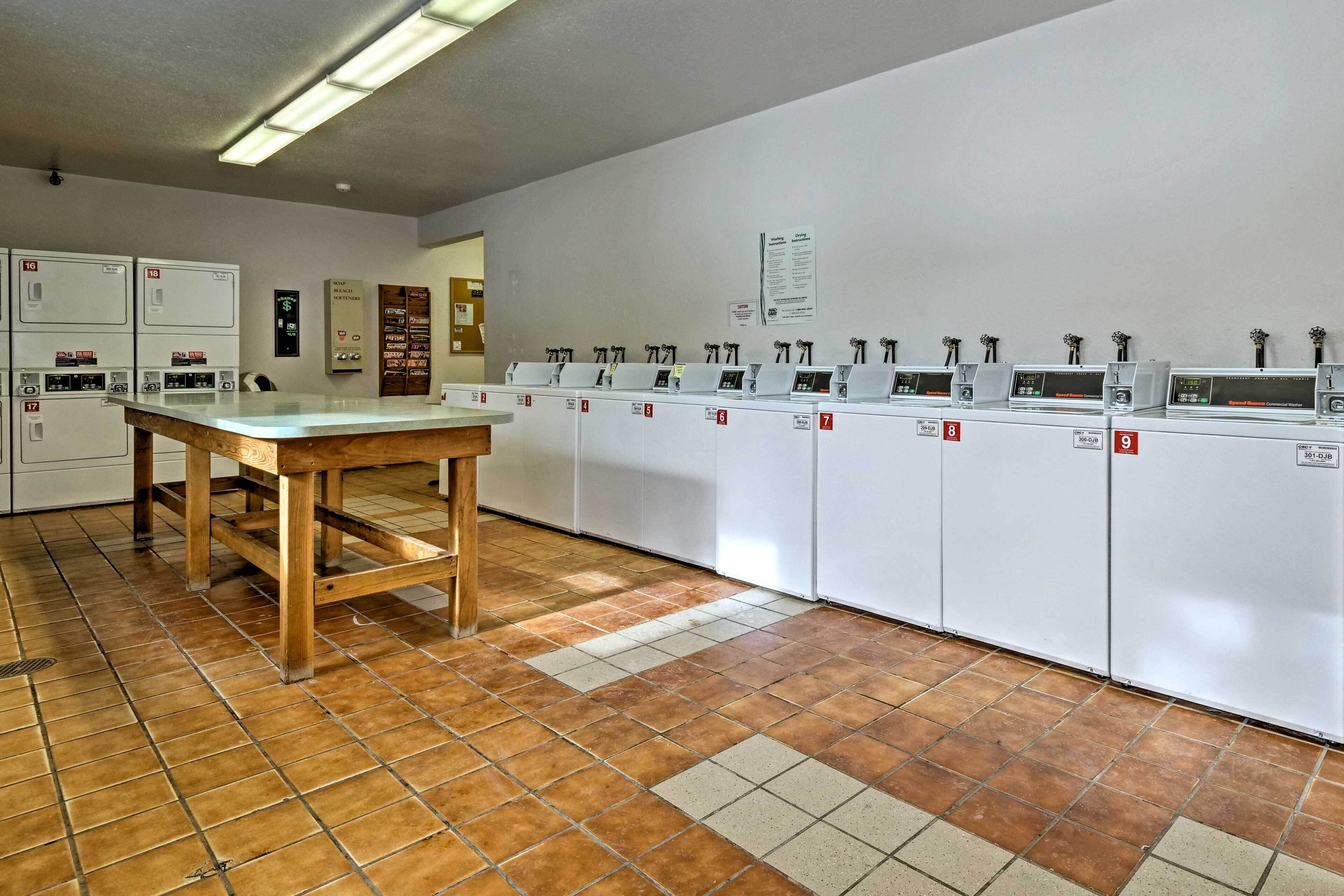 A laundry facility with multiple washing machines and dryers, a wooden table, and a tiled floor.