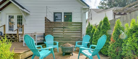 A patio with four turquoise Adirondack chairs, a fire pit, and a wooden deck leading to a house with a white exterior and a wooden fence.