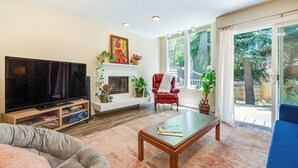 A living room with a flat-screen TV, a fireplace, a red armchair, and a large window with a view of trees. - Beautiful Boulder Townhome: Walk to CU & Pearl St! (Boulder)