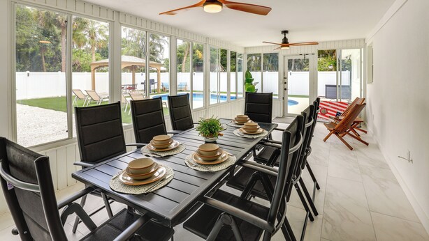 A dining area with a long table set for six, surrounded by chairs, with a ceiling fan above. - Vero Beach Vacation Rental: Pool & Putting Green! (Vero Beach)