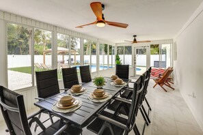 A dining area with a long table set for six, surrounded by chairs, with a ceiling fan above. - Vero Beach Vacation Rental: Pool & Putting Green! (Vero Beach)