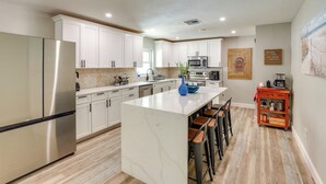 A modern kitchen with white cabinets, stainless steel appliances, and a marble island with bar stools. - Vero Beach Vacation Rental: Pool & Putting Green! (Vero Beach)
