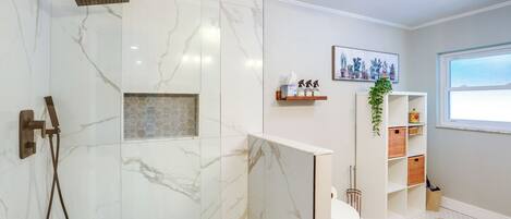 A modern bathroom with a shower, toilet, and a shelf with toiletries.