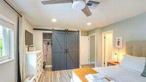 A bedroom with a bed, a ceiling fan, a sliding barn door closet, a washing machine, and a bedside table with a lamp. - Vero Beach Vacation Rental: Pool & Putting Green! (Vero Beach)