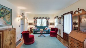 Un salon avec un canapé bleu, des fauteuils rouges, un meuble en bois et un grand miroir.