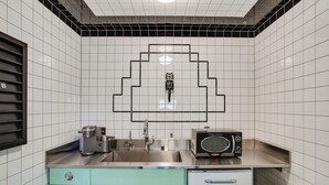 Une cuisine avec des murs recouverts de carreaux blancs, un évier en acier inoxydable, un four à micro-ondes et un réfrigérateur.