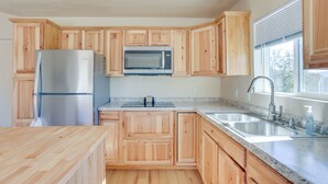 A modern kitchen with wooden cabinets, a stainless steel refrigerator, a microwave, a sink, and a window with blinds. - Comfy Oakhurst Duplex Near Hiking & Sightseeing! (Oakhurst)