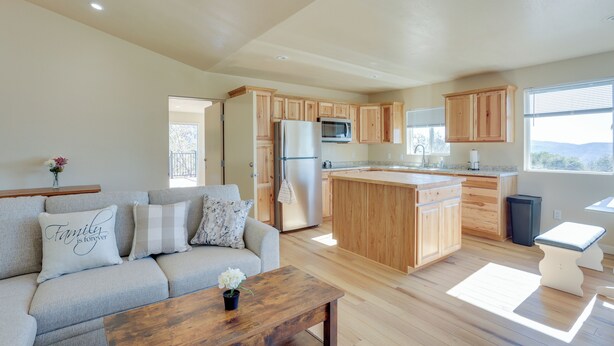 A spacious living area with a sofa, wooden cabinets, a kitchen island, and a view of the outdoors. - Comfy Oakhurst Duplex Near Hiking & Sightseeing! (Oakhurst)