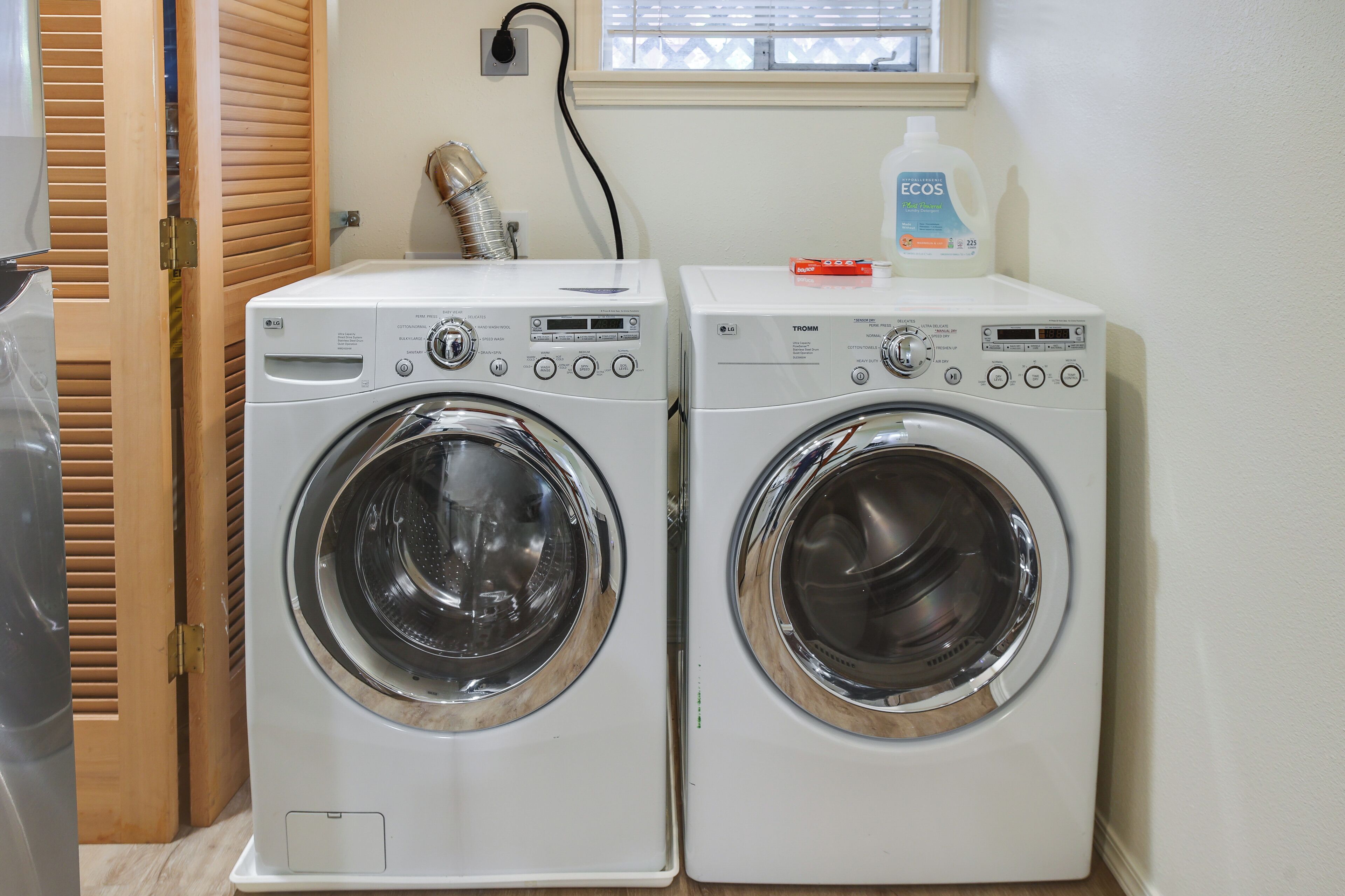 Two front-loading washing machines in a laundry room with a wooden door and a window.