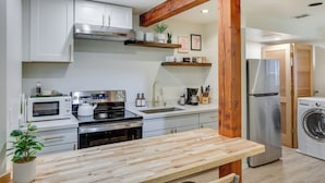 A modern kitchen with white cabinets, a wooden countertop, stainless steel appliances, and a wooden beam ceiling. - Updated Tacoma Home w/ Fire Pit! (Tacoma)