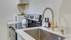 A kitchen with a stainless steel sink, a white countertop, a microwave, a stove, and a gold faucet. - Updated Tacoma Home w/ Fire Pit! (Tacoma)