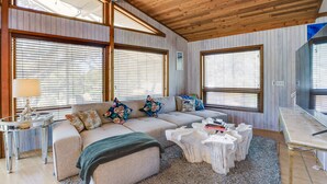 A spacious living area with a large beige sectional sofa, a coffee table, and a dining table. There are large windows with blinds, a lamp, and a decorative sculpture on a side table. - Scenic Siesta Key Home ~ 1 Mi to Village & Beach! (Siesta Key)